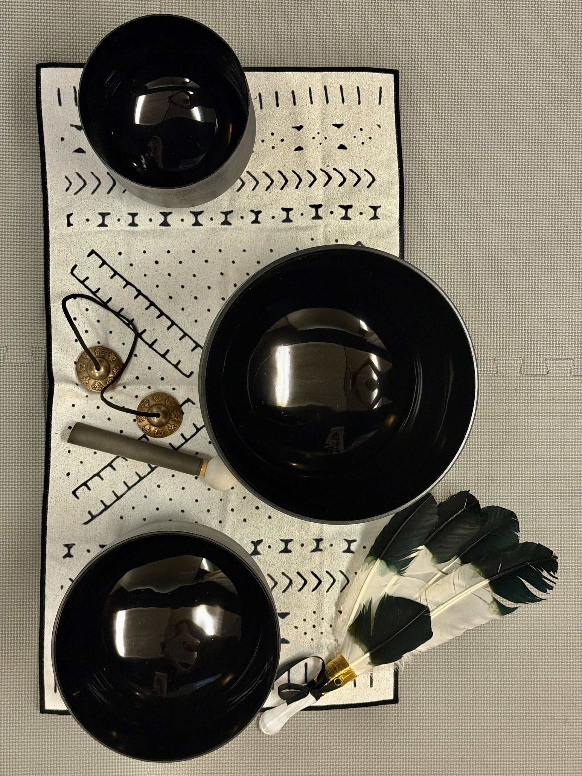 Three black bowls on a decorative mat with feathers and a chime.