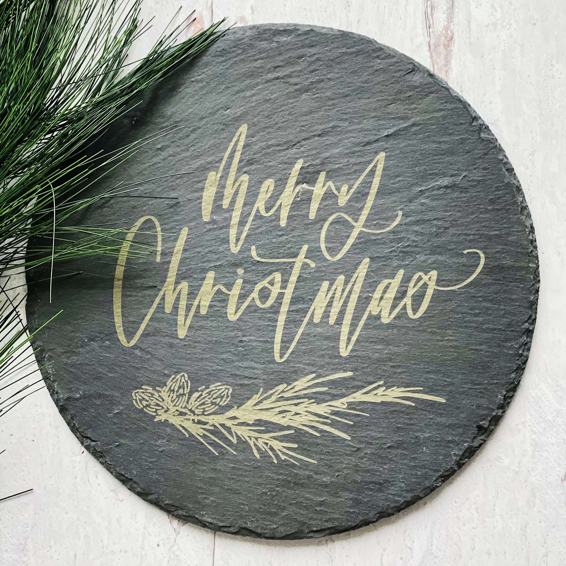 12" round slate tray with merry christmas and a pine sprig engraved in the center